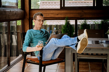 Man wearing glasses using laptop, sitting in cozy armchair on the terrace