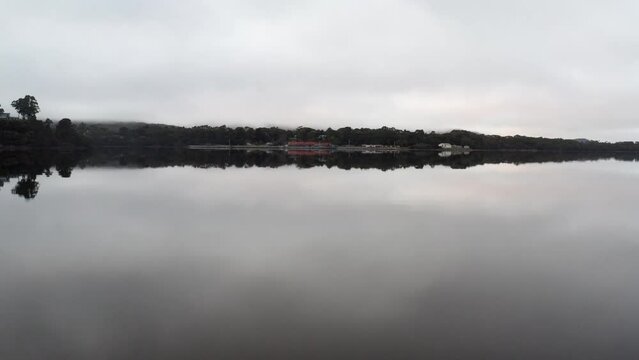 Aerial: Drone flying low over a perfectly still lake towards the coast near Strahan, Tasmania