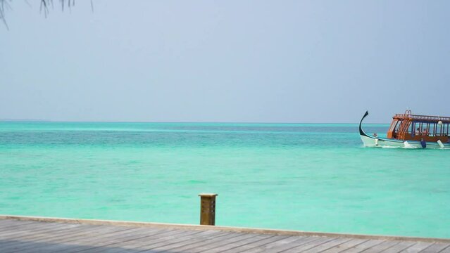 Maldivian wooden boat moving across bay of blue water to dock