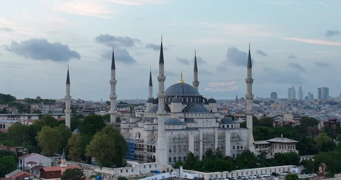 Establishing orbiting aerial drone shot of a Hagia Sophia Holy Grand Mosque with Bosphorus bridge and city skyline with a flag on the background in Fatih, Istanbul, Turkey at sunset.