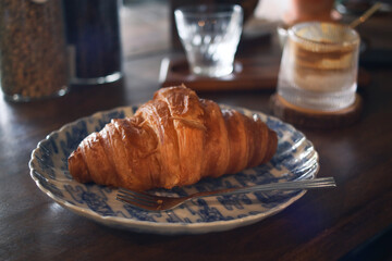 Close up of French nature butter croissant in a plate with fork, coffee in background .It's a buttery, flaky pastry made with a yeast leavened dough that laminated with butter in multiple layers