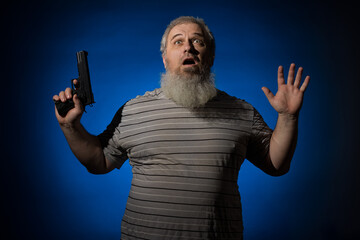 A gray-haired, bearded, disheveled, adult man in a striped shirt, with a weapon in his hand. He is disarmed and raised his hands up. Self defense concept. On a blue background. - obrazy, fototapety, plakaty