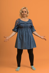 a plus size blonde woman in a blue dress spread her arms to the sides in disbelief on a colored background