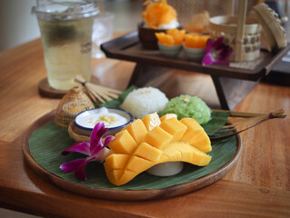 A plate of ripe mango with sticky rice and coconut milk sauce with a cup of ice tea, various sweet...