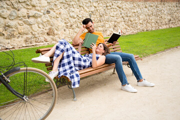 Fototapeta premium Woman lying in the lap of her couple reading a book in a park
