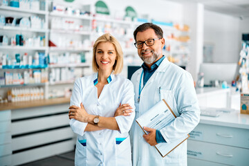 Portrait of confident pharmacist and her mature coworker in pharmacy and looking at camera.