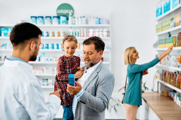 Father and daughter buying in drugstore with help of pharmacist.