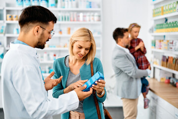 Mid adult woman chooses medicine with help of pharmacist in drugstore.