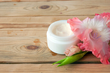 Obraz na płótnie Canvas cosmetic cream and gladiolus flowers bunch on wooden background. Organic cosmetic concept. Natural cosmetic cream with flower extract