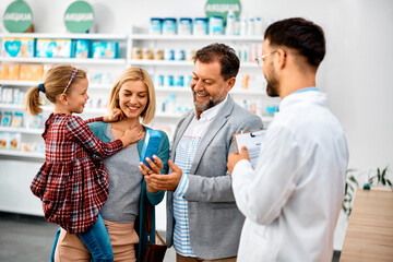 Happy family choosing product with help of pharmacist in drugstore.