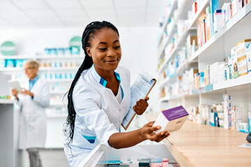 Young smiling black pharmacist going through inventory in pharmacy.