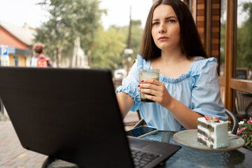 women in outdoor cafe working on laptop. Woman using a computer with a cup of coffee in hands.