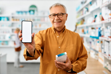Close up of senior man showing blank screen on smart phone while buying medicine in drugstore.