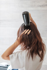 Fototapeta premium young woman using hair dryer at home or hotel. Hairstyles and lifestyle concepts