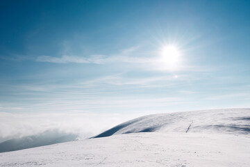 The sun over a snowy mountain slope. A trail running along a snow-covered mountain slope.