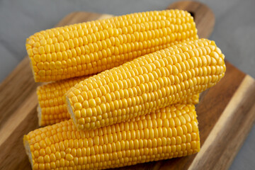Fresh Raw Organic Yellow Sweet Corn on a wooden board on a gray background, side view. Close-up.