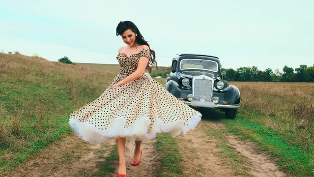 happy smiling sexy woman in pin-up style clothes dancing, spinning, waving skirt in motion. Vintage polka dot white dress red high heels. road green grass summer nature. Girl fashion model retro lady