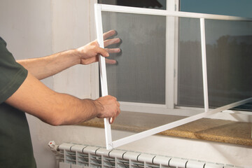 Man installing the mosquito net on the window.