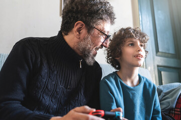 Happy family playing video games - father and son having fun sitting on the sofa playing videogames together and holding joypad - technology and people lifestyle concept