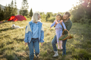 Fototapeta premium Young caucasian couple with little girl have fun while travel in the mountains. Happy family spending summer vacation at campsite. Father tossing daughter in his arms