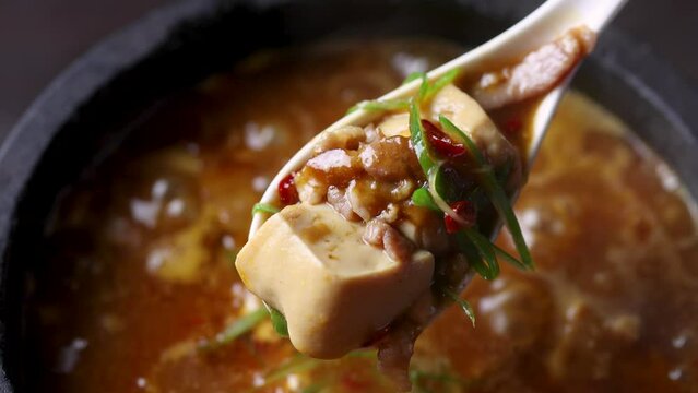 煮え立つ石鍋から豆腐を掬い上げ、とろとろで熱々な質感を閉じ込めた「麻婆豆腐動画」。レンゲから溢れる濃厚なルウの輝きが際立つシーンで、辛口メニューや本格中華の販促に最適な高品質素材です。 | Lifting sizzling hot Mapo Tofu with a spoon from a stone pot.