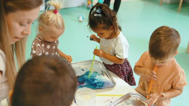 Multi-cultural nursery school. Toddlers playing with striped straws and milk painting, using nontoxic food coloring for colors. Creative kids activity for using their senses and brain development