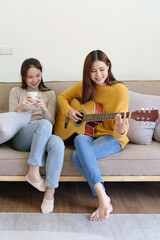 LGBTQ, female couple playing guitar happily on the sofa in the house.