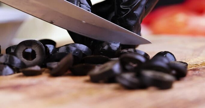 Cut black olives into pieces while cooking a salad, black olives are pitted and cut into pieces on a cutting board