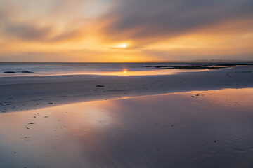 Long exposure of a hazy sunset over a sandy beach and reflections in a large pool of water