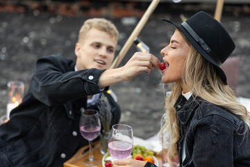 Beautiful young loving couple on a surprise date on a Saint Valentine's Day on a rooftop. Romantic picnic with candles. Newlyweds. Panoramic view, urban cityscape. Modern wedding boho style
