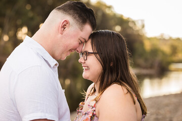 Young man and woman boyfriend and girlfriend foreheads touching laughing with water in background