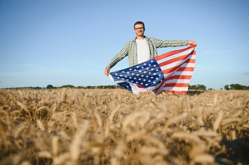Young man holding American flag, standing in wheat field
