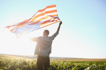 A young farmer stands with a USA flag in a soybean field. The concept of the US agricultural industry.