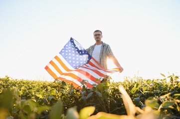 A young farmer stands with a USA flag in a soybean field. The concept of the US agricultural...