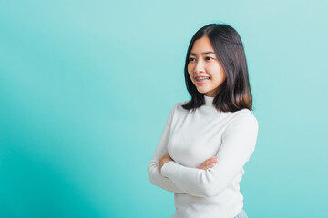 Young beautiful Asian woman smiling with crossed arms, Portrait of positive confident female stand cross one's arm, studio shot isolated on a blue background - obrazy, fototapety, plakaty