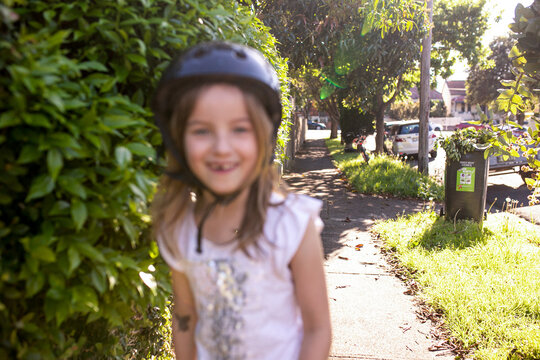 Out Of Focus Girl With A Helmet On The Side Walk With Trees And Hedge On The Sides