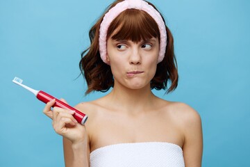 a thoughtful, funny woman stands in a white towel facing the camera, holding a toothbrush in her hand, biting her lower lip. Horizontal studio photography with empty space