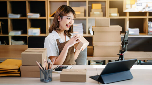 .Beautiful asian woman blogger showing clothes in front of camera to recording vlog video live streaming at her shop. Online Shopping concept..