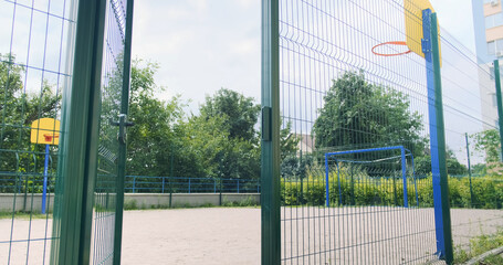 Basketball hoop behind the fence, courtyard of a residential area. Multi-storey residential buildings, green trees, bushes. Kyiv, Ukraine.
