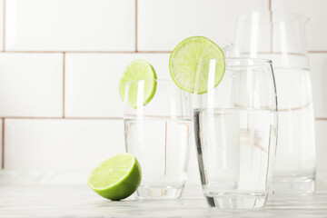 Glass and jug with fresh water and lime on marble table. Space for text
