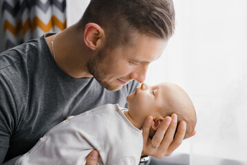 Fototapeta premium Portrait of a young Caucasian father keeping his newborn son at home.