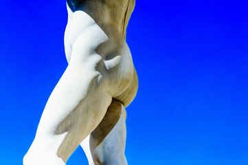 Monochrome of a naked man statue with a blue sky in the background on a sunny day