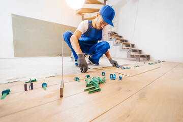Adult repairman in a special uniform laying tiles with tile leveling system on the floor in a new house