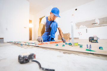 Adult repairman in a special uniform laying tiles with tile leveling system on the floor in a new house