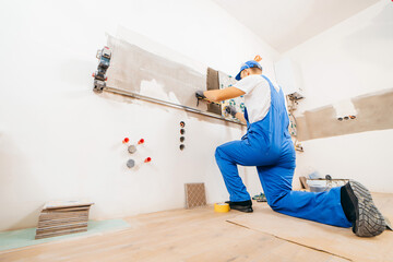 Adult repairman in a special uniform laying tiles with tile leveling system at wall on kitchen in a...