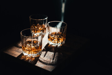 Glass with whiskey on wooden table and black background. Copy space.