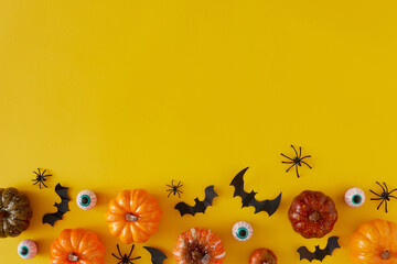 Creative holiday horror concept with bats, eyeballs, pumpkins and spiders on yellow background with copy space. Spooky idea. Halloween minimal concept.