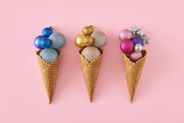 Three ice cream cone with Christmas tree balls on isolated pastel pink background, top view photo....