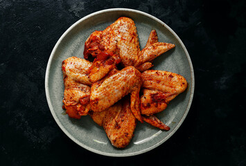 Raw chicken wings marinated in paprika and curry. Copy space. Raw meat in a plate. Dark background,...