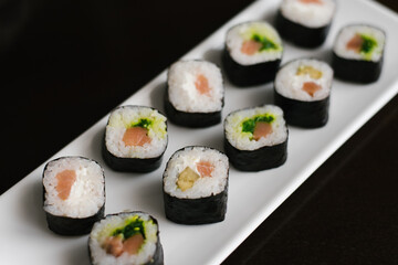 Rolls with cheese and salmon on a white rectangular plate on a dark background.